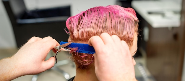 Peluquería cortes de pelo corto rosa mojado teñido de joven mujer caucásica peinar con un peine en una peluquería.