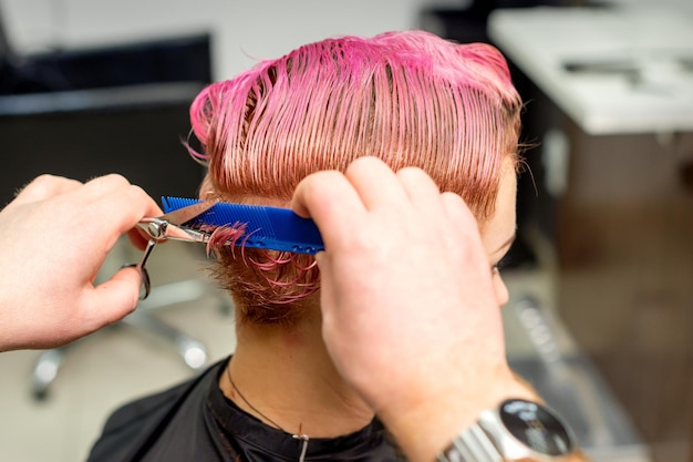 Peluquería cortes de pelo corto rosa mojado teñido de joven mujer caucásica peinar con un peine en una peluquería.