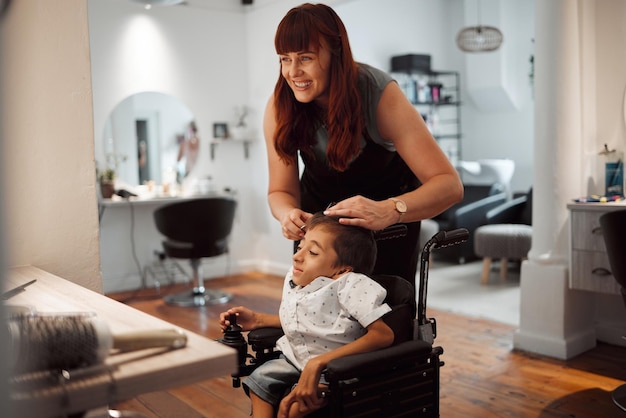 Peluquería y discapacidad para niños en silla de ruedas en salón o barbería Mujer estilista y feliz por el servicio a niños discapacitados con parálisis cerebral en tienda o pequeña empresa