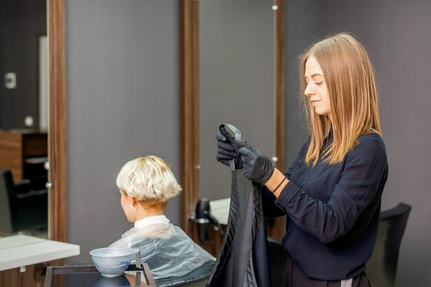 Peluquería femenina se prepara se pone una capa negra sobre la clienta en un salón de belleza