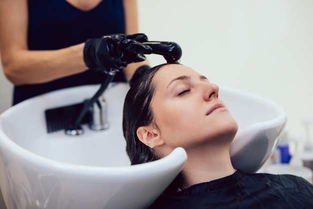 Peluquería lavando el cabello de una hermosa joven en peluquería.