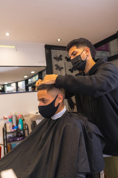 Peluquería con mascarilla cortando el cabello de un cliente joven