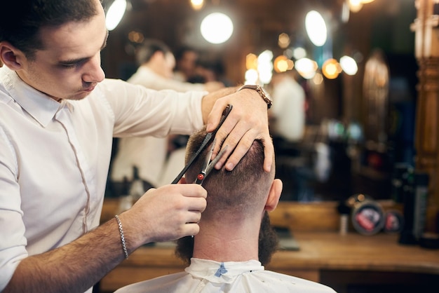 Peluquería masculina haciendo un corte de pelo corto para el cliente en una barbería moderna Concepto de corte de pelo tradicional con tijeras