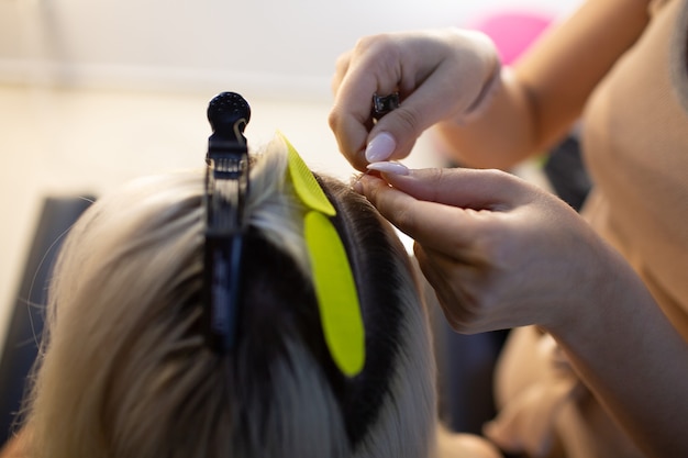 Peluquería mujer haciendo extensiones de cabello a mujer joven con cabello rubio en salón de belleza. Extensión de cabello profesional.