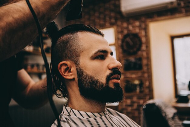 Peluquería Primer plano del maestro de corte de pelo del hombre hace el peinado en la peluquería Peluquería barbudo musculoso fuerte corta el pelo largo y negro del cliente