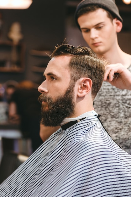 Peluquería profesional cortando el cabello del joven barbudo en peluquería