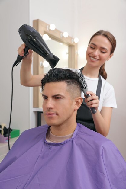 Peluquería profesional que seca el cabello del cliente en el salón