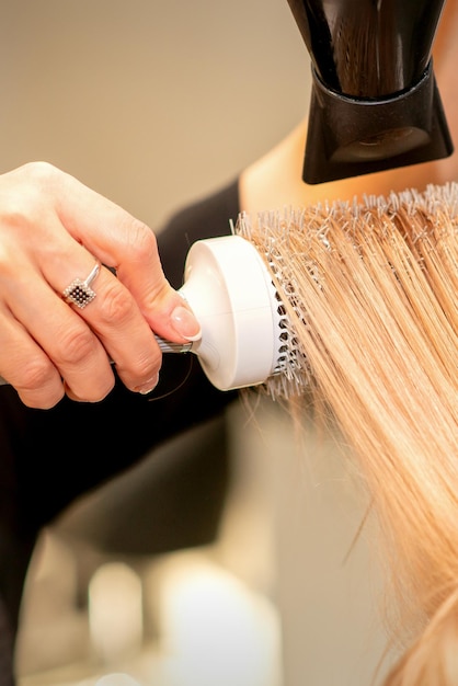 Peluquería profesional seca el cabello con secador de pelo y cepillo redondo en un salón de belleza.