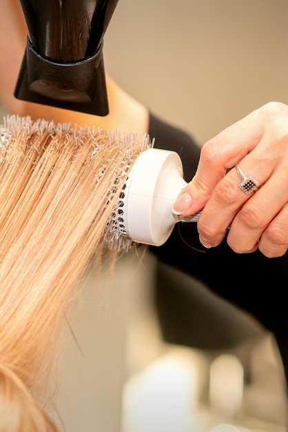 Peluquería profesional seca el cabello con secador de pelo y cepillo redondo en un salón de belleza.