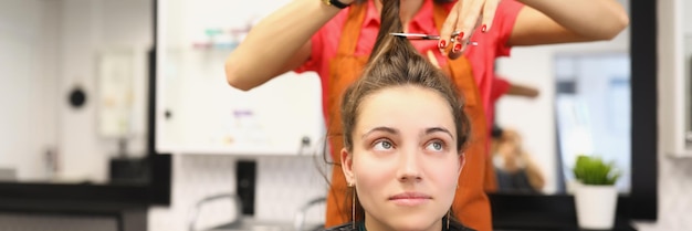 Peluquería profesional sosteniendo un mechón de pelo y cortando con una herramienta de tijeras