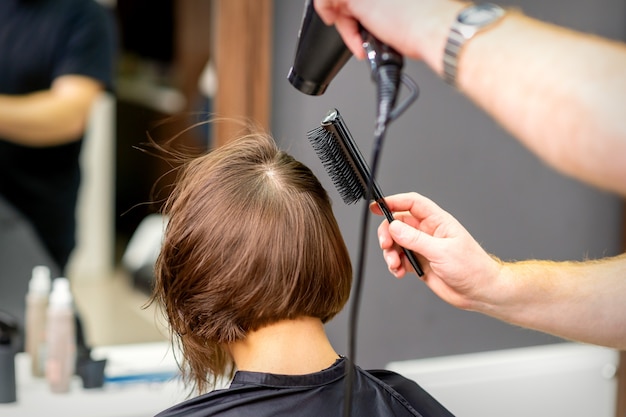 Peluquería seca el cabello castaño de la joven en un salón de belleza