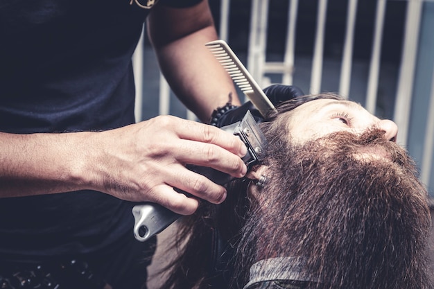 Peluquero con afeitadora para cortar la barba de un hombre.