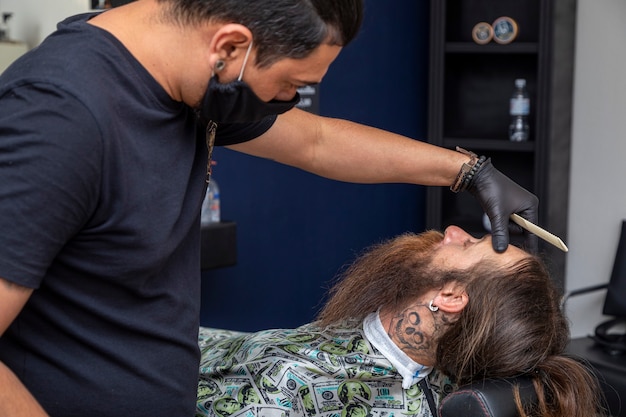 Peluquero con afeitadora para cortar la barba de un hombre.