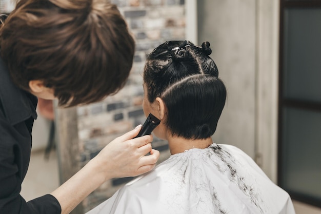 El peluquero alisa el cabello de la niña después de un corte de pelo corto.