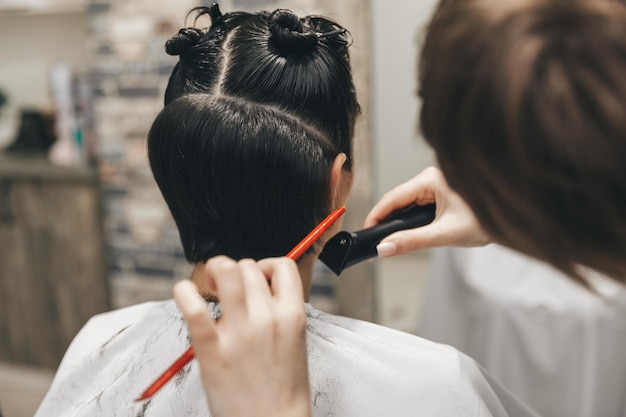 El peluquero alisa el cabello de la niña después de un corte de pelo corto.