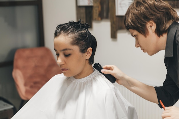 El peluquero alisa el cabello de la niña después de un corte de pelo corto.