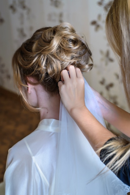 Peluquero arregla un velo en el pelo de novia de la boda