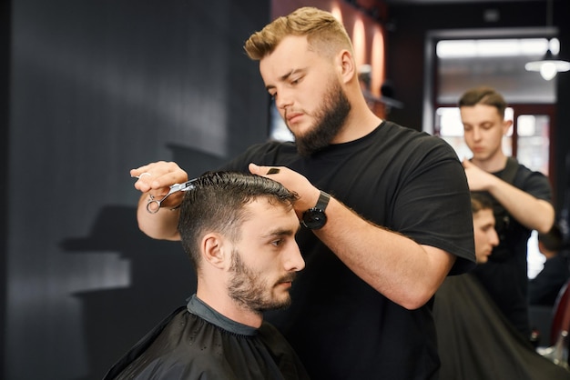 Peluquero arreglando el cabello de un cliente masculino que en un salón moderno