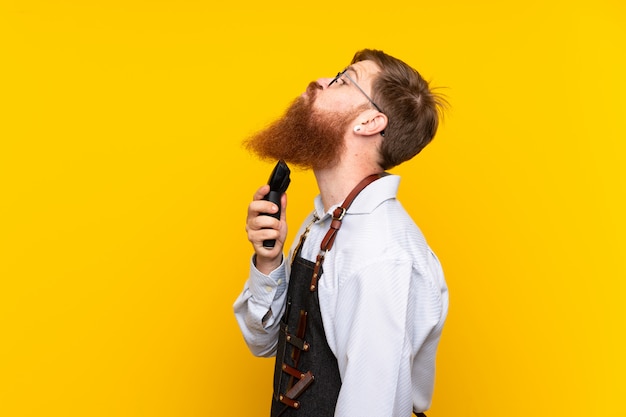 Peluquero con barba larga en un delantal sobre pared amarilla aislada