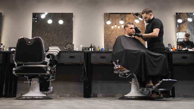 Peluquero barbudo cortando el cabello de un cliente masculino