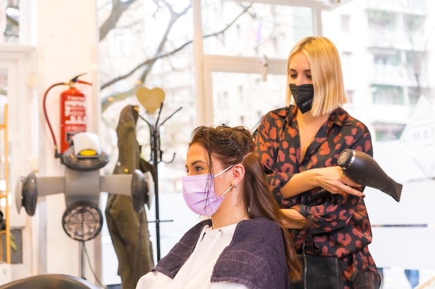 Peluquero caucásico con máscara de protección facial realizando un peinado al cliente Medidas de seguridad en la pandemia de Covid19 una nueva normalidad