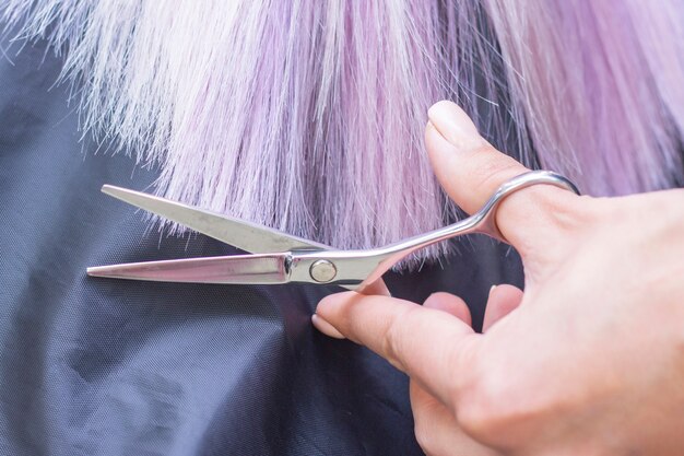 El peluquero le corta el cabello a una chica con cabello largo y rubio. Peluquería manos sosteniendo tijeras