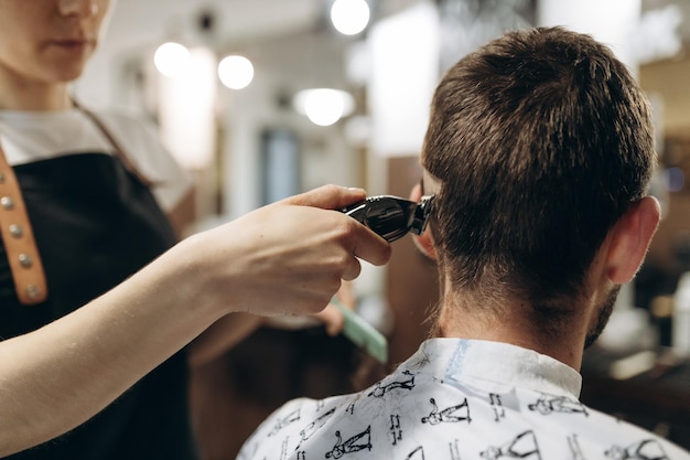 Un peluquero corta a un joven con un cortapelos peinándose el pelo en la cabeza Trabajo del maestro en el corte de pelo de los hombres en una barbería