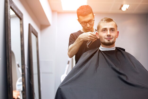 peluquero corta el pelo de un joven en una barbería