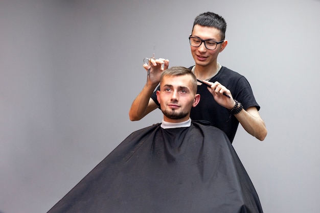 peluquero corta el pelo de un joven en una barbería