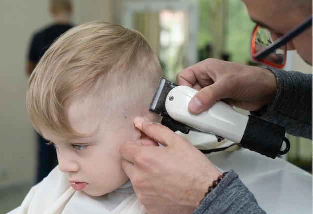 El peluquero corta el pelo de un niño rubio en la peluquería
