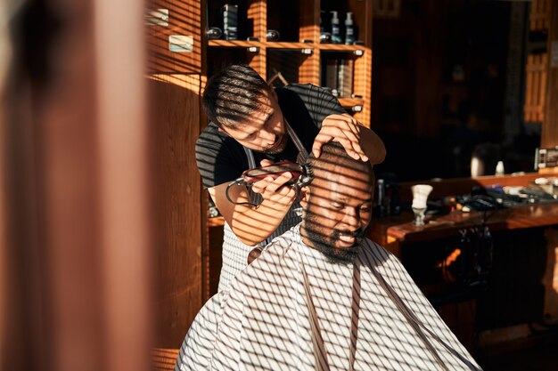 Peluquero cortando el cabello del cliente con cortadora de cabello eléctrica profesional