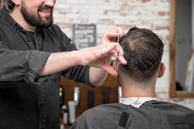 Peluquero cortando el pelo con tijeras a un joven apuesto Fotografía de alta calidad