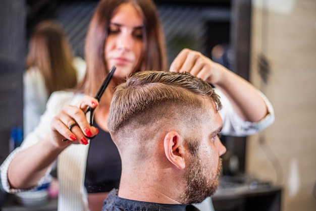 Peluquero cortando con tijeras hombre barbudo en barbería