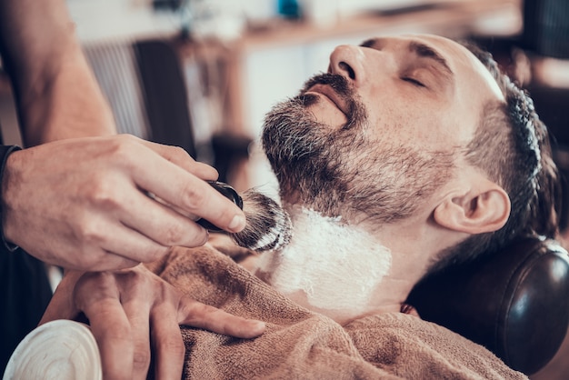 Peluquero está cepillando espuma de afeitar en la cara del hombre.