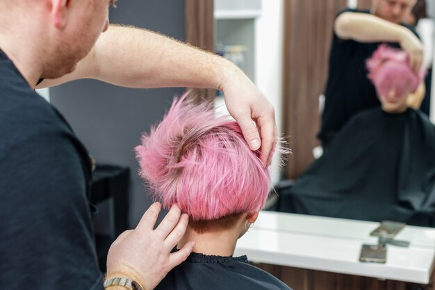 El peluquero está comprobando el peinado rosado de la mujer joven.