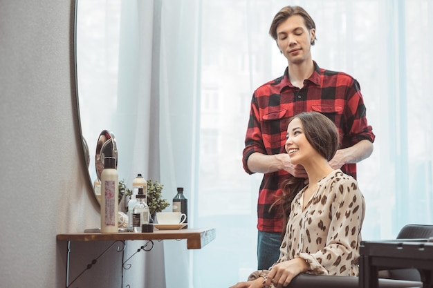 Peluquero estilista que peina el cabello largo para una hermosa joven asiática en el momento de trabajo del salón de belleza