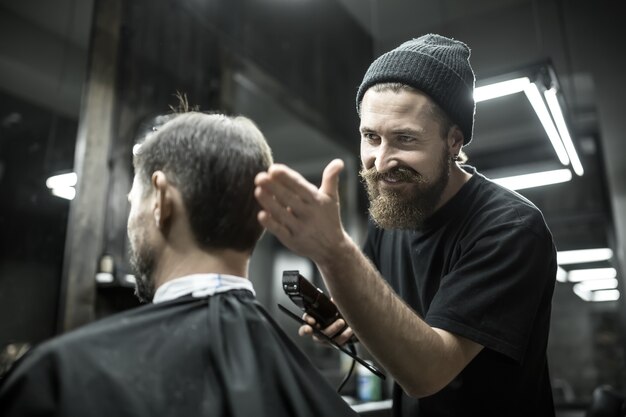 Peluquero feliz con barba mira el cabello de su cliente en la barbería