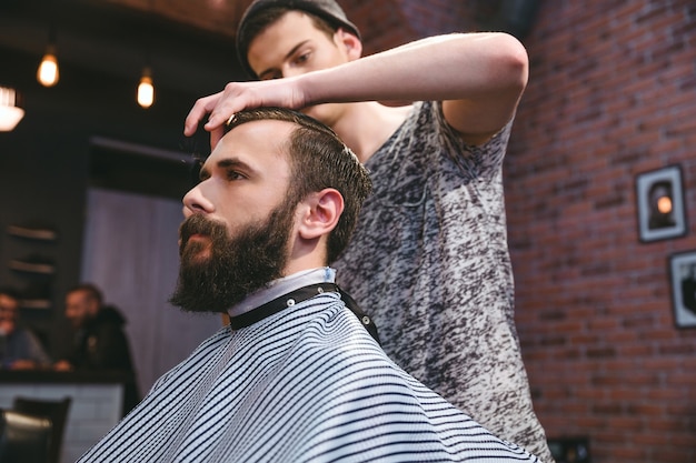 Peluquero guapo joven cortando el pelo de hipster barbudo atractivo joven en peluquería