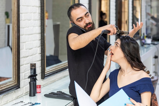 Peluquero hablando por teléfono y dando forma al cabello de su cliente Foto de alta calidad