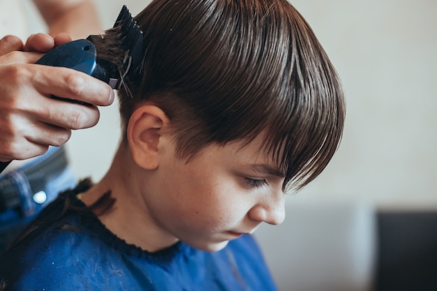 Peluquero hace un corte de pelo con cortapelos para un niño