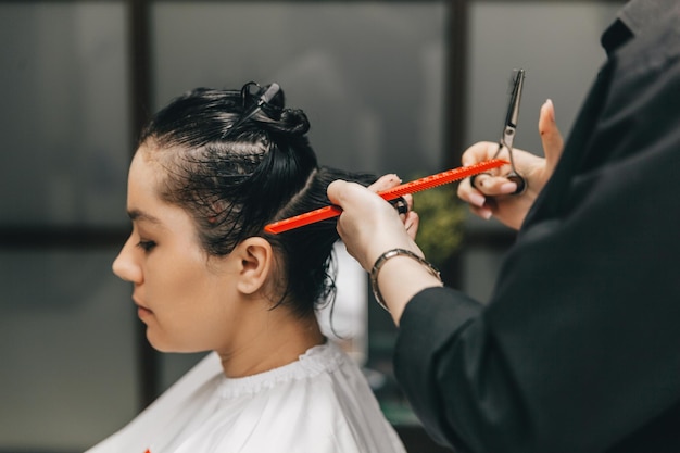 El peluquero hace un corte de pelo a una mujer en el salón El peluquero corta el cabello mojado peinándose con un peine cliente con vista posterior de cabello corto
