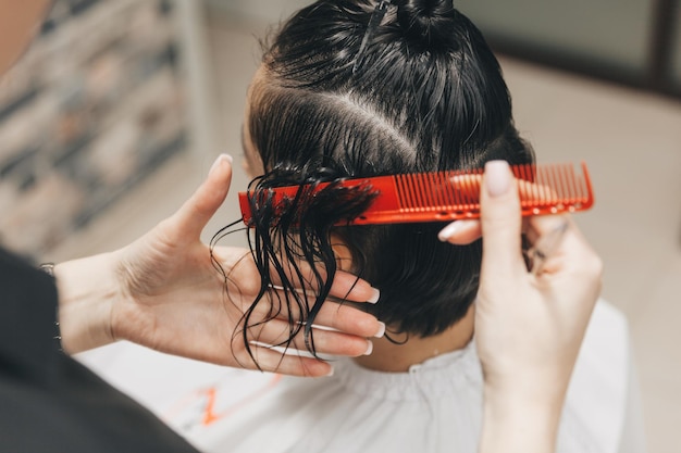 El peluquero hace un corte de pelo a una mujer en el salón El peluquero corta el cabello mojado peinándose con un peine cliente con vista posterior de cabello corto