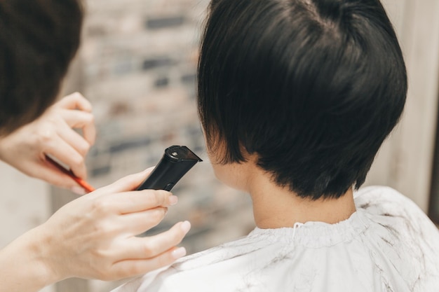 El peluquero hace un corte de pelo a una mujer en el salón El peluquero corta el cabello mojado peinándose con un peine cliente con vista posterior de cabello corto