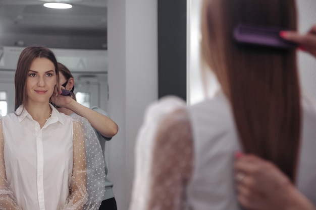 Peluquero hace peinado linda mujer joven y bonita en salón de belleza. El servicio al cliente en la habitación interior crea una imagen increíble. Asistente de creación de peinados de trabajo. Estilo de concepto, satisfacción. Copia espacio