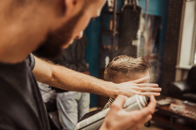 Peluquero hace un peinado para un niño en una barbería.