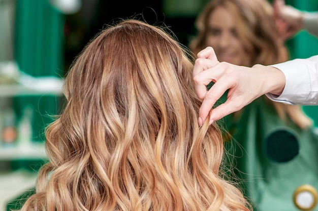 Peluquero hace peinado rizado para mujer en salón de belleza, vista posterior.