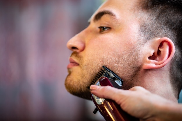 Peluquero hacer corte de pelo de barba con cortapelos en barbería