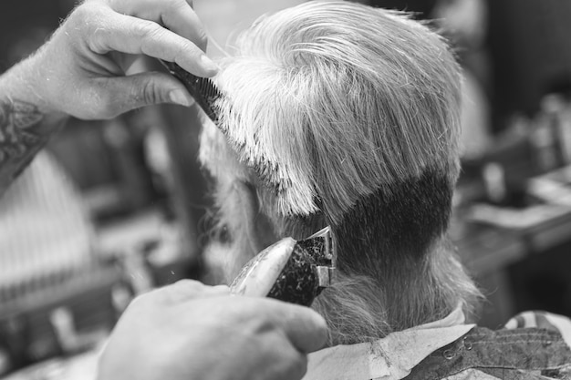 Peluquero haciendo elegante corte de pelo para anciano en la barbería