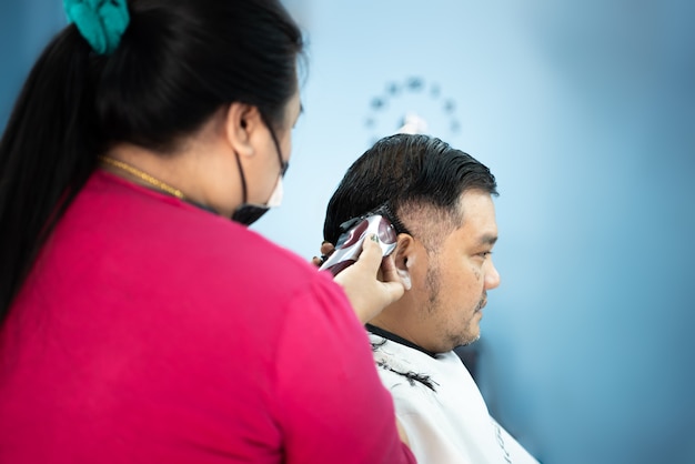 Peluquero de hombre asiático no identificado o corte de pelo de peinado un cliente de cuerpo regordete de hombre en peinado de moda en peluquería