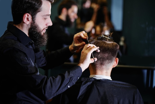 El peluquero un hombre con barba corta al cliente con unas tijeras en la barbería